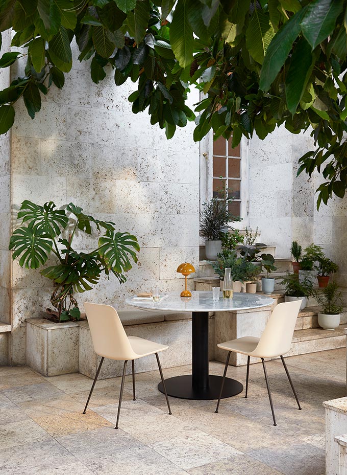 A lifestyle image of an outdoor setting with the Flowerpot VP9 lamp in orange featured on a round marble top table. Image: &Tradition.