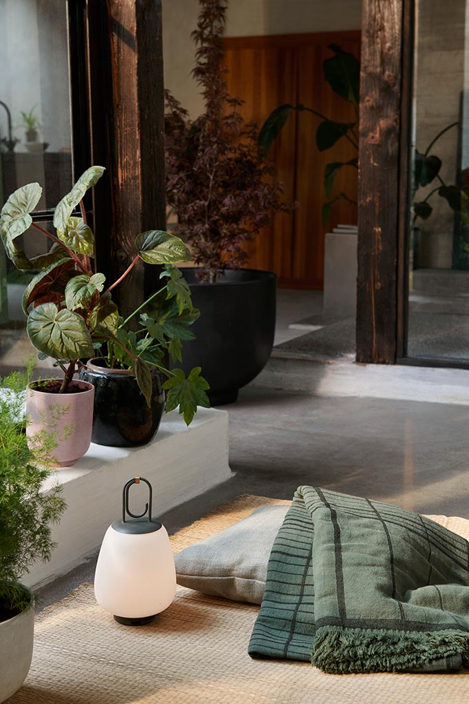 A lifestyle image of the Lucca SC51 lamp on a beige rug next to planters. Image: &Tradition.