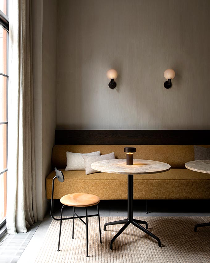 A lifestyle image of a built-in sofa with tables in front and the Column table lamp featured on top of one. Image: MENU.