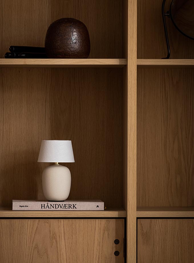 A lifestyle image of a close up on a bookcase featuring the Torso lamp atop a book. Image: MENU.