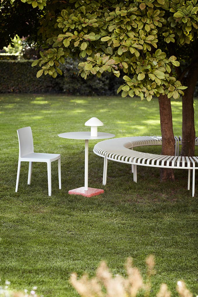 A garden with the Pallisade park bench surrounding a tree and the Pao portable table lamp on a round table next to it. Image: HAY.