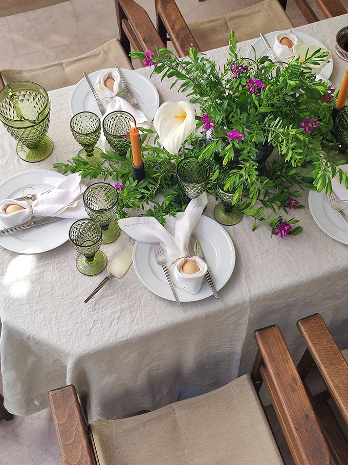 Bird's eye view of an Easter lunch tablescape with an organic vibe and lots of greenery stretched across the table.
