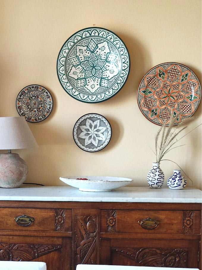 Detail of a vintage sideboard with a marble top styled with a gallery of pattern ceramic platters.