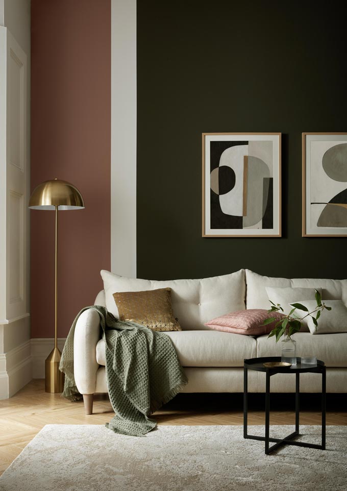 Partial view of a sophisticated muted colored sitting room with an off white sofa against a dark olive green and terracotta wall. Image via: Sofology.